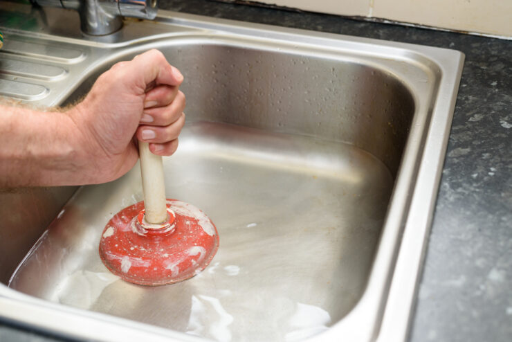 Man holding a plunger with one hand and water in sink, used to clean a clogged / blocked kitchen sink