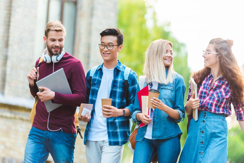 portrait of smiling multiethnic students with backpacks walking in park